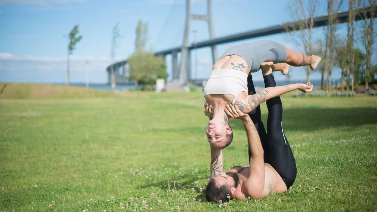 A couple performing acro yoga in a sunny park, showcasing strength and balance.