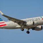 American Airlines Airbus A319 airplane landing under clear sky in New York City.