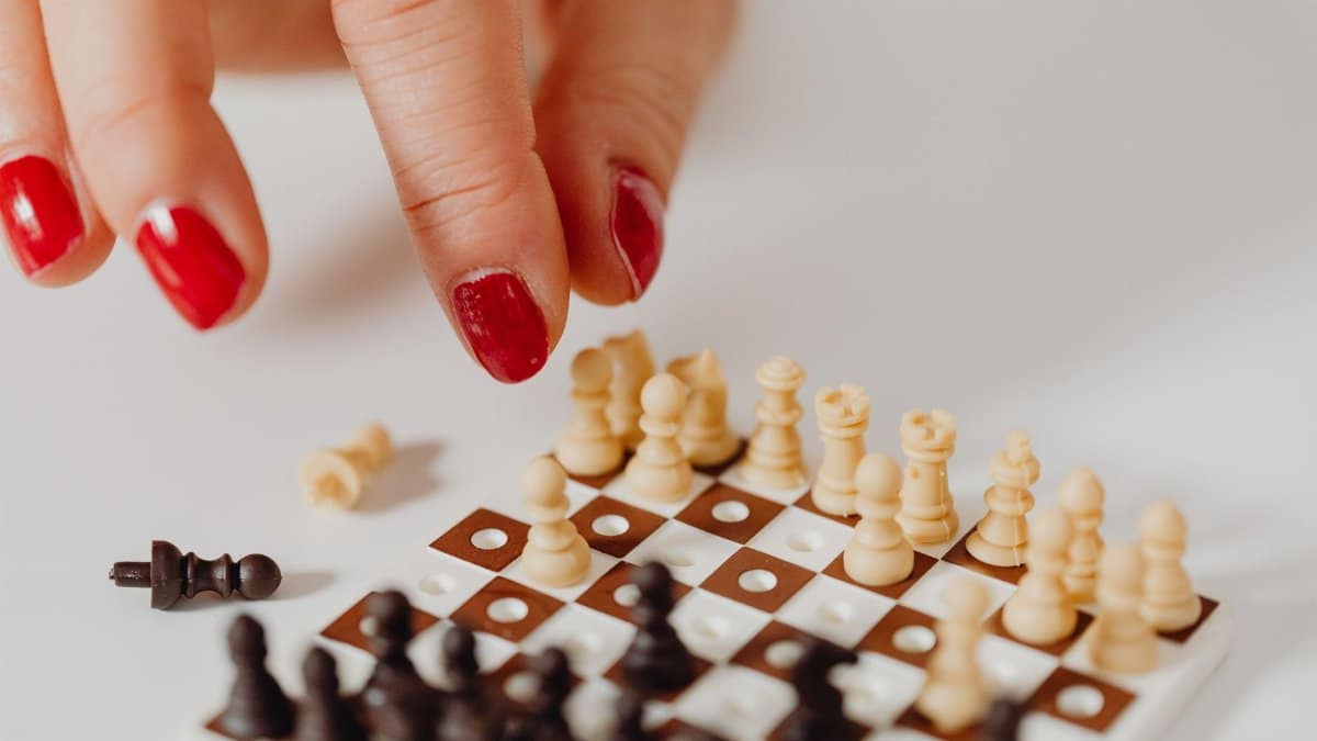 Red manicured hand playing on a small chessboard, showcasing strategy in detail.