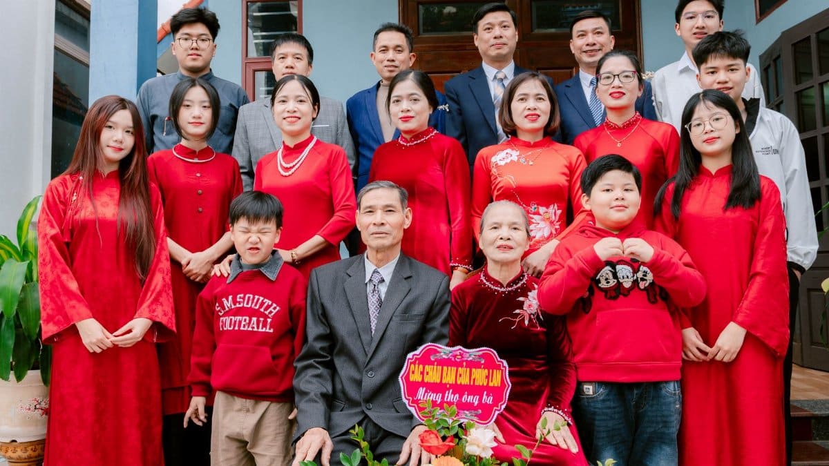 Large family gathering wearing traditional red outfits for a celebration, posing outdoors.