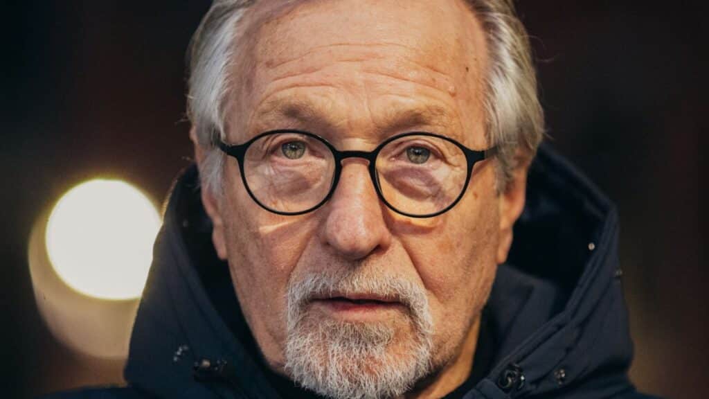 Portrait of a senior man with glasses and beard in a hooded jacket.