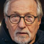 Portrait of a senior man with glasses and beard in a hooded jacket.