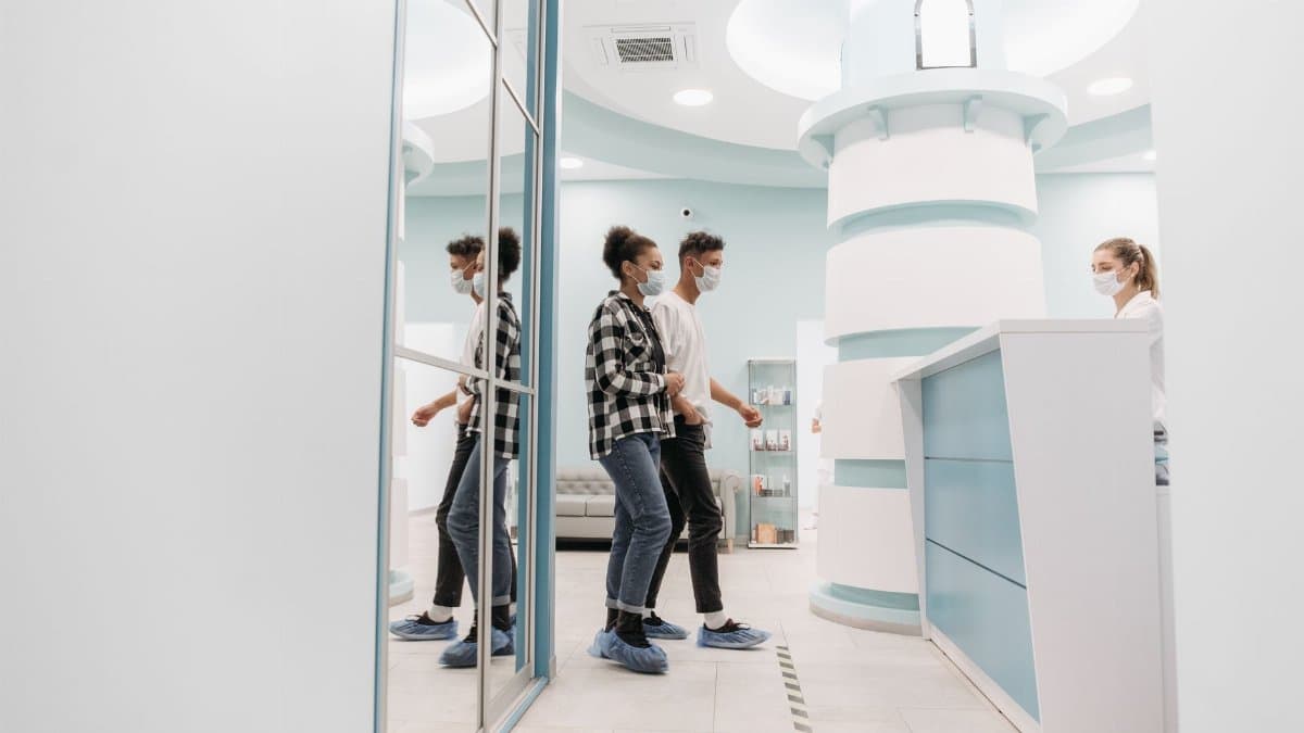 Visitors wearing face masks standing at a modern clinic reception desk.