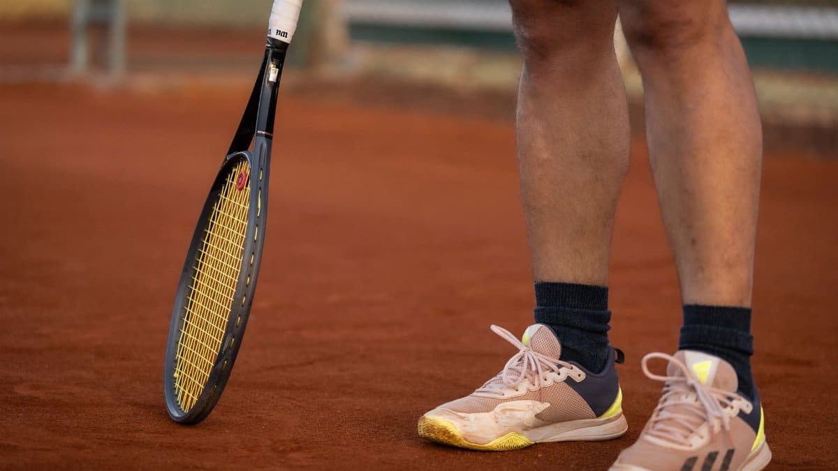 A close-up shot featuring a tennis racket and player's shoes on a clay tennis court.