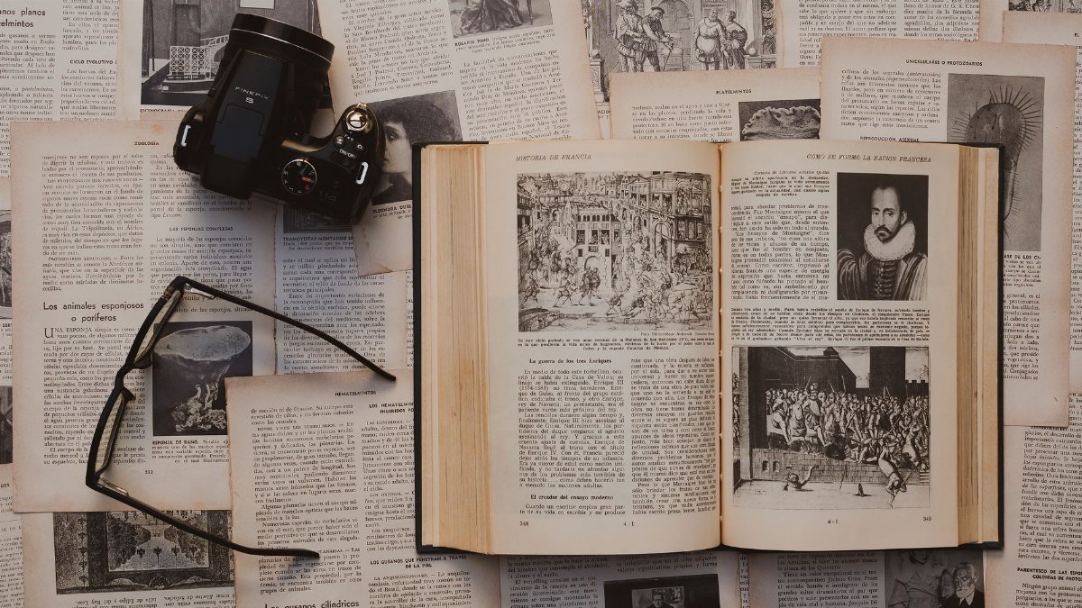 Flat lay of a vintage book, camera, and glasses on historical text pages, evoking nostalgia and learning.