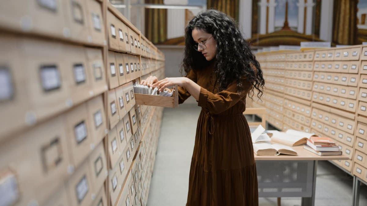 A woman browsing a card catalog in library archives, focusing on research and information gathering.