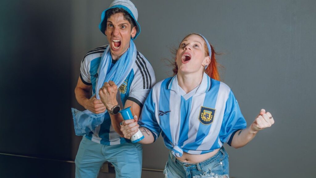 Young Argentina soccer fans in jubilant celebration with joyful expressions indoors.