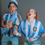 Young Argentina soccer fans in jubilant celebration with joyful expressions indoors.