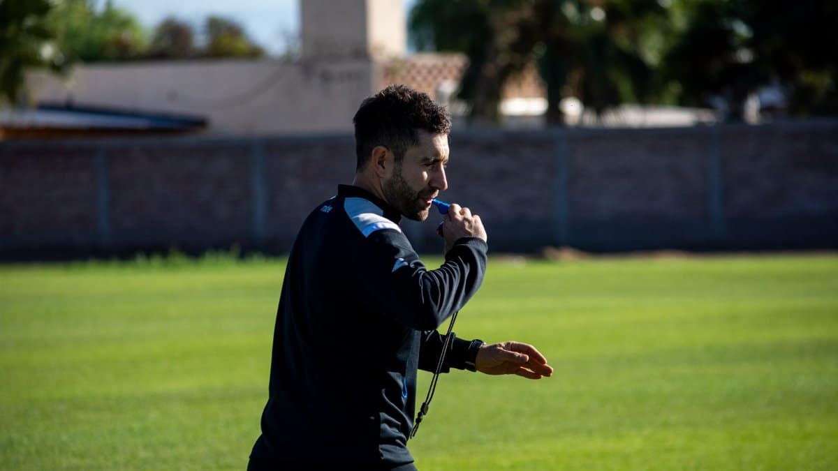 Football coach blowing a whistle during practice on a sunny day outdoors.