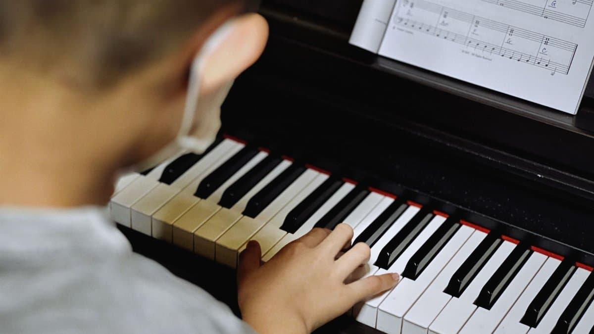 Young child learning to play piano with open sheet music, focusing on keys.