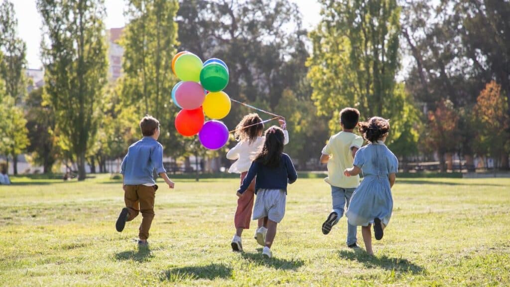 Children happily running with balloons in a sunny park, capturing friendship and joy.