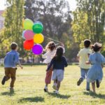 Children happily running with balloons in a sunny park, capturing friendship and joy.