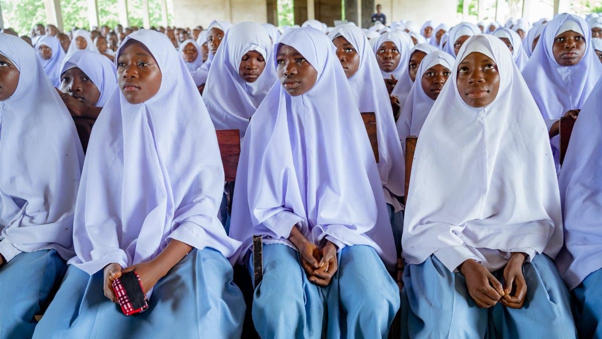 A group of students dressed in traditional hijabs attending a school assembly indoors.