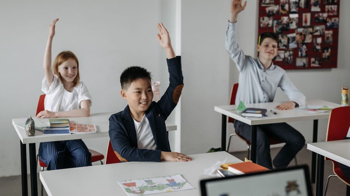 Diverse group of students actively participating in a classroom setting, raising hands for recitation.
