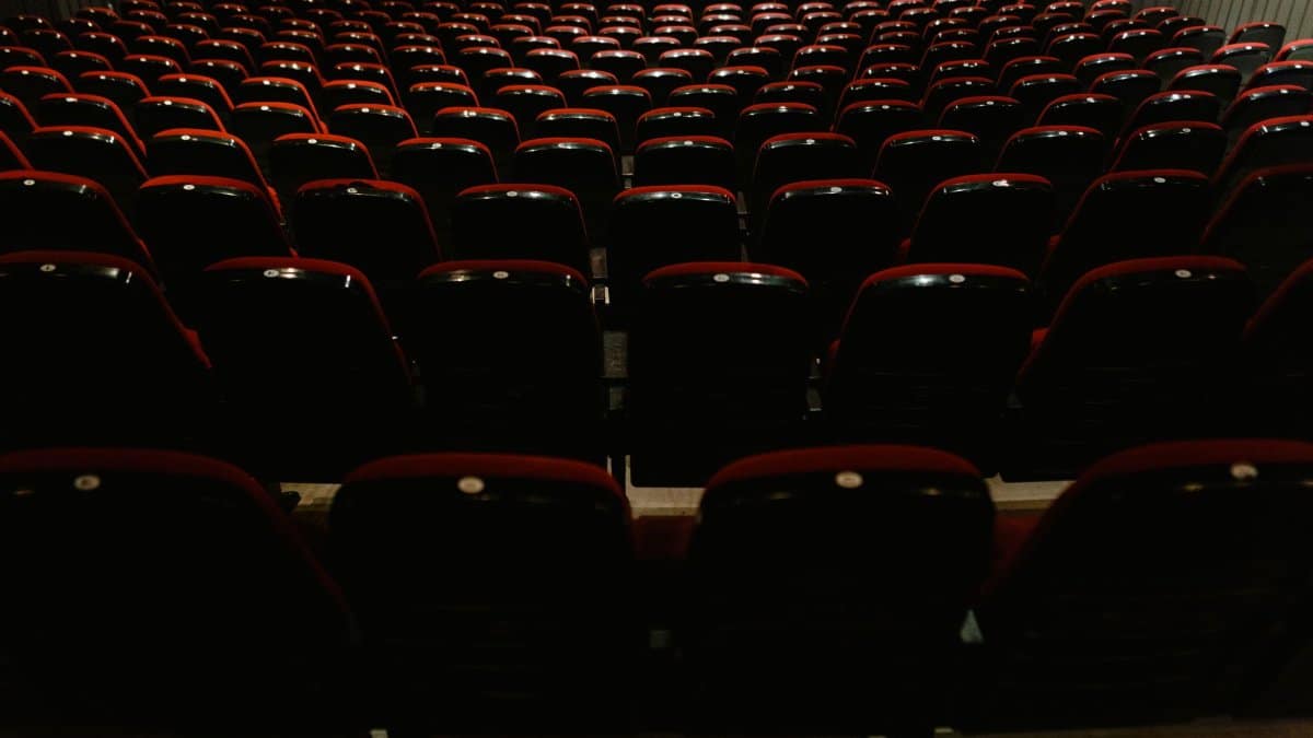 An empty movie theater interior with rows of red and black seats, awaiting audience.