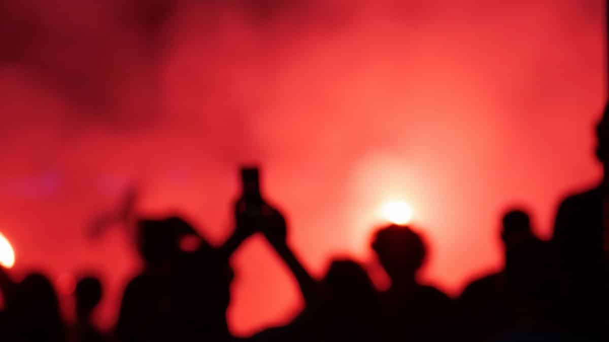 A vibrant scene depicting silhouettes of a crowd against a red smoke-filled background, capturing the essence of an electrifying night event.