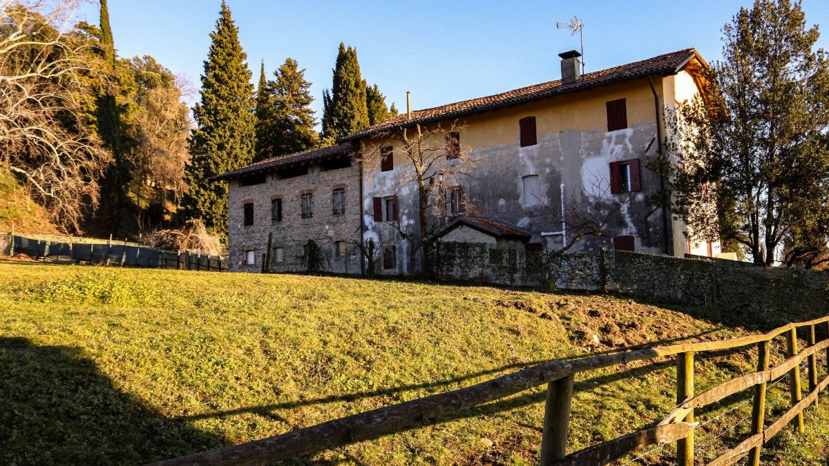 Charming old farmhouse in scenic countryside, surrounded by trees and a wooden fence.