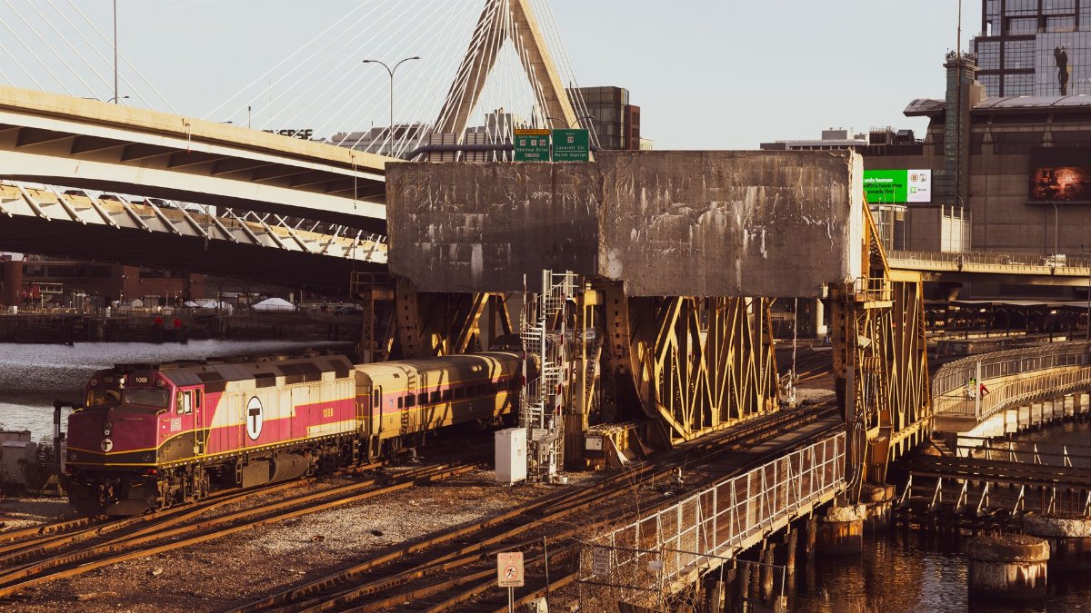 A train passes under the Leonard P. Zakim Bunker Hill Memorial Bridge in Boston during sunset.