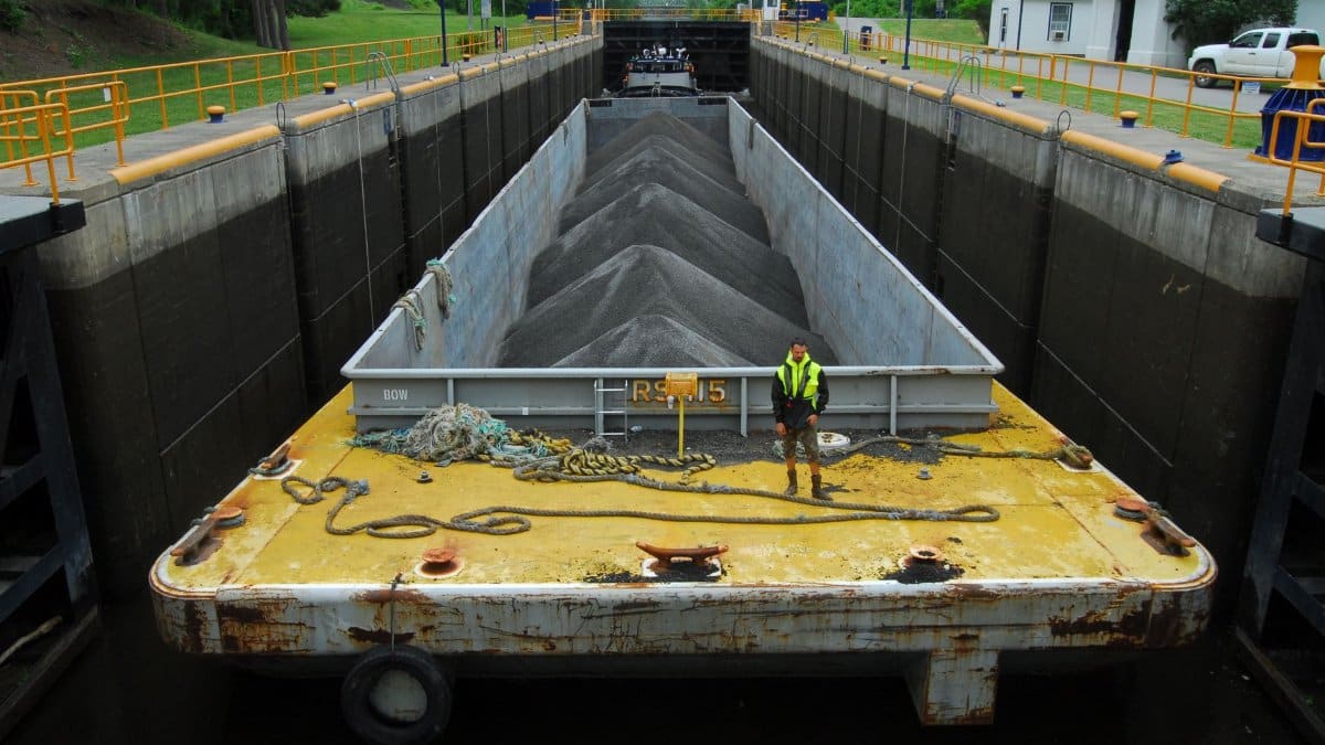 Cargo barge loaded with material in a river lock system with industrial surroundings.