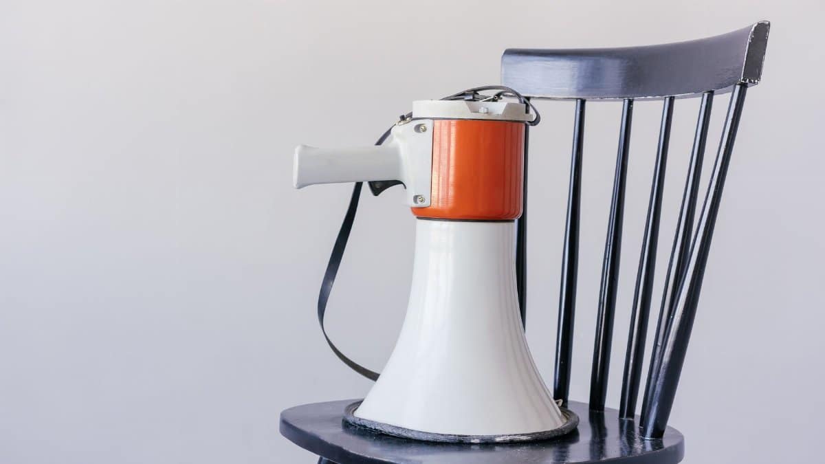 Close-up of a megaphone placed on a black wooden chair against a neutral background.