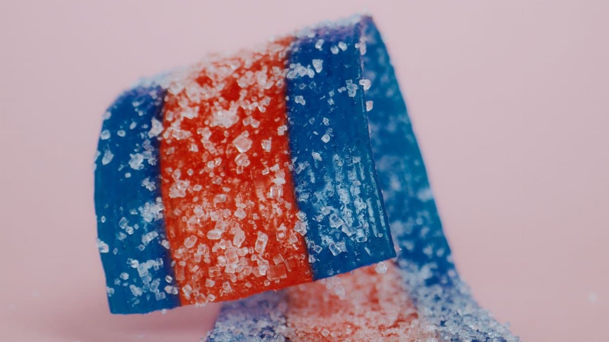 Close-up of vibrant red and blue sugared candy strips on a pink background, highlighting their texture.