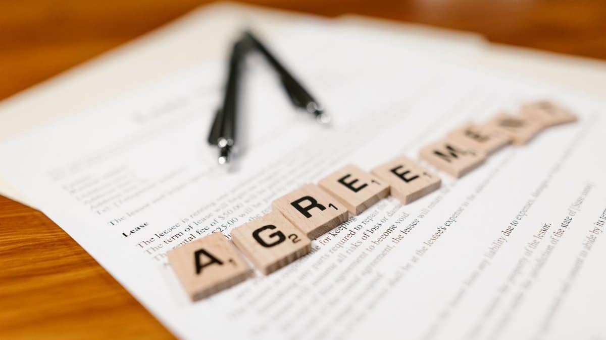 Scrabble tiles spelling 'AGREEMENT' on a lease document, emphasizing contractual themes.