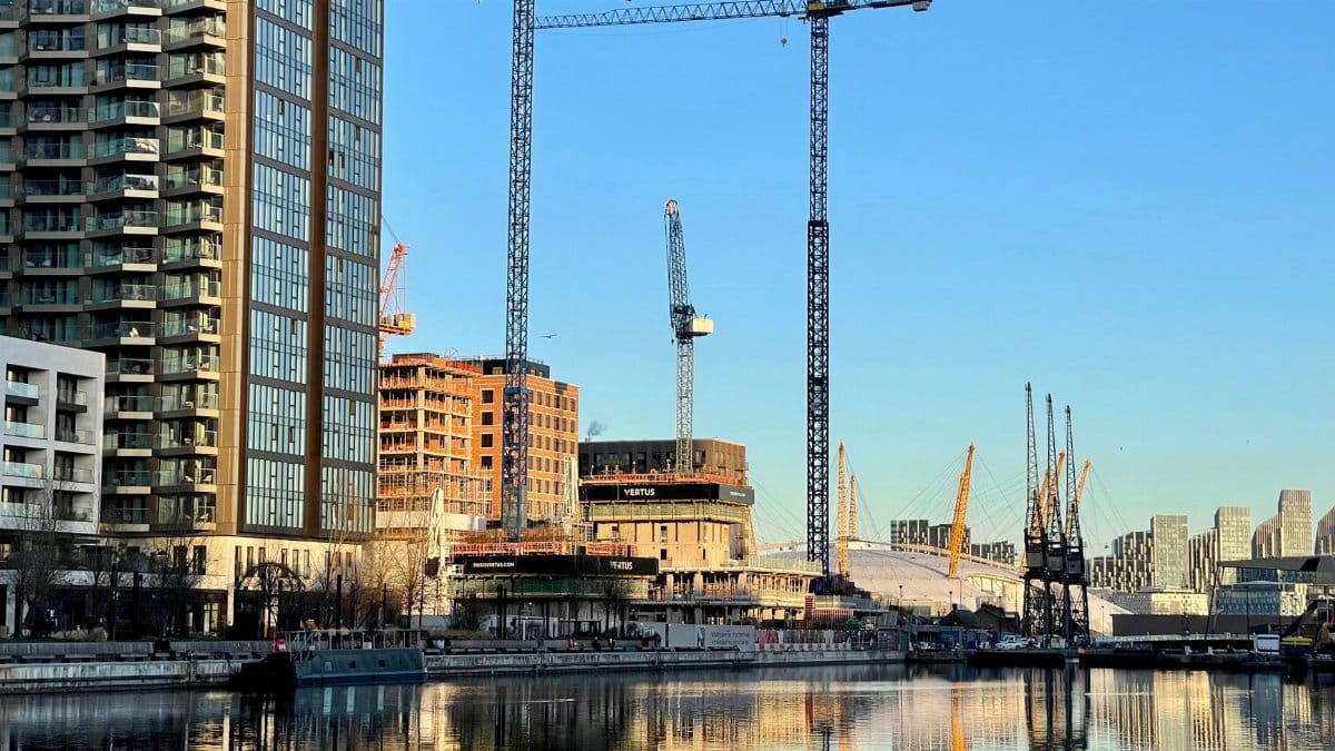 Urban skyline featuring skyscrapers and construction cranes on a clear day by the waterfront.
