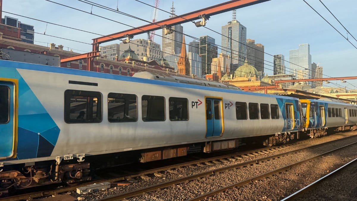 Melbourne train station with city skyline in background, featuring a commuter train under clear skies.