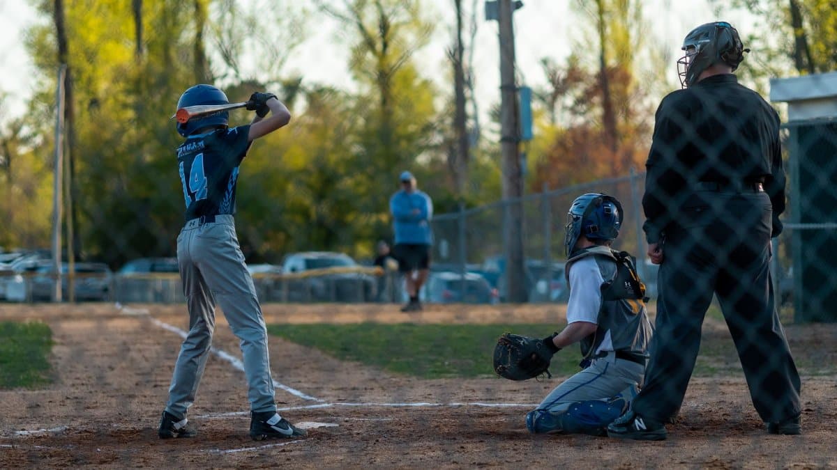 A young baseball player at bat during a lively spring game with catcher and umpire ready.