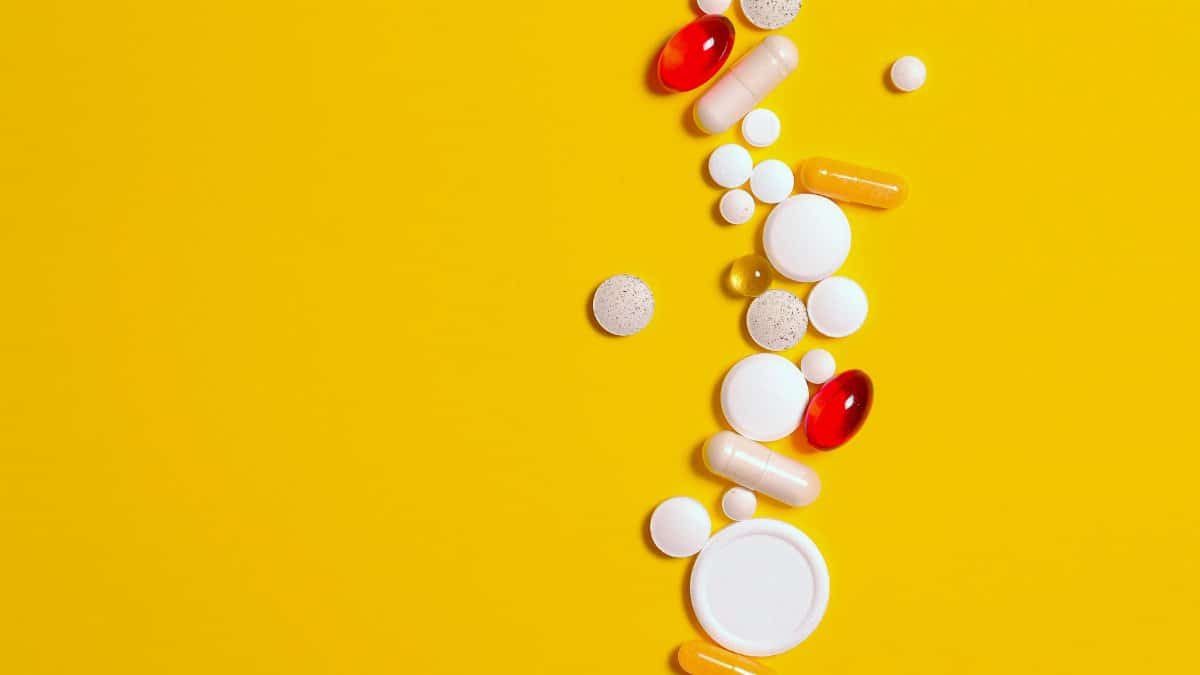 Assorted pills and capsules scattered on a bright yellow background, representing healthcare and medication.
