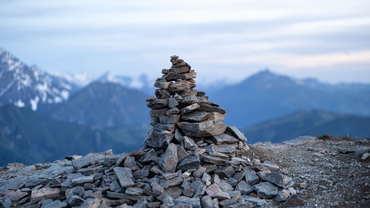 A tranquil stone cairn stands against a majestic alpine mountain backdrop, symbolizing respect and guidance.
