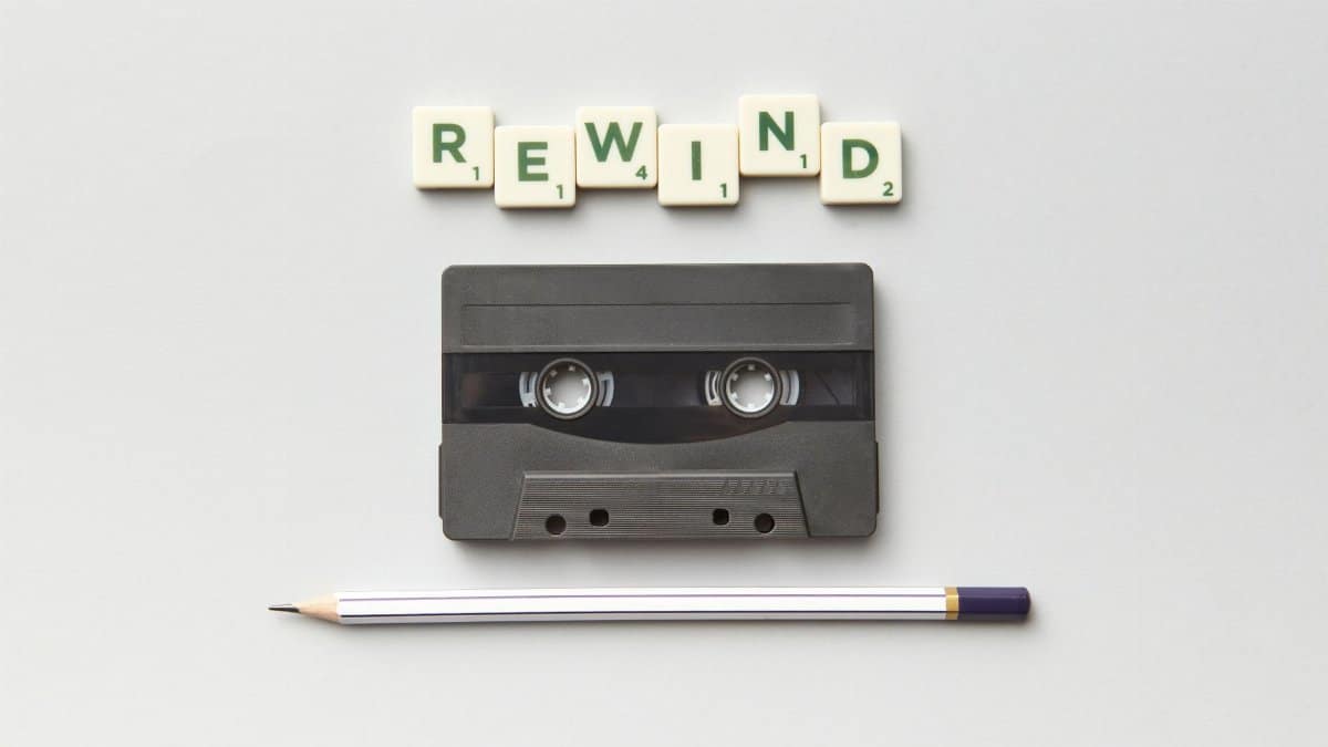 Minimalist flat lay of a cassette tape, pencil, and 'REWIND' tiles, evoking nostalgia.