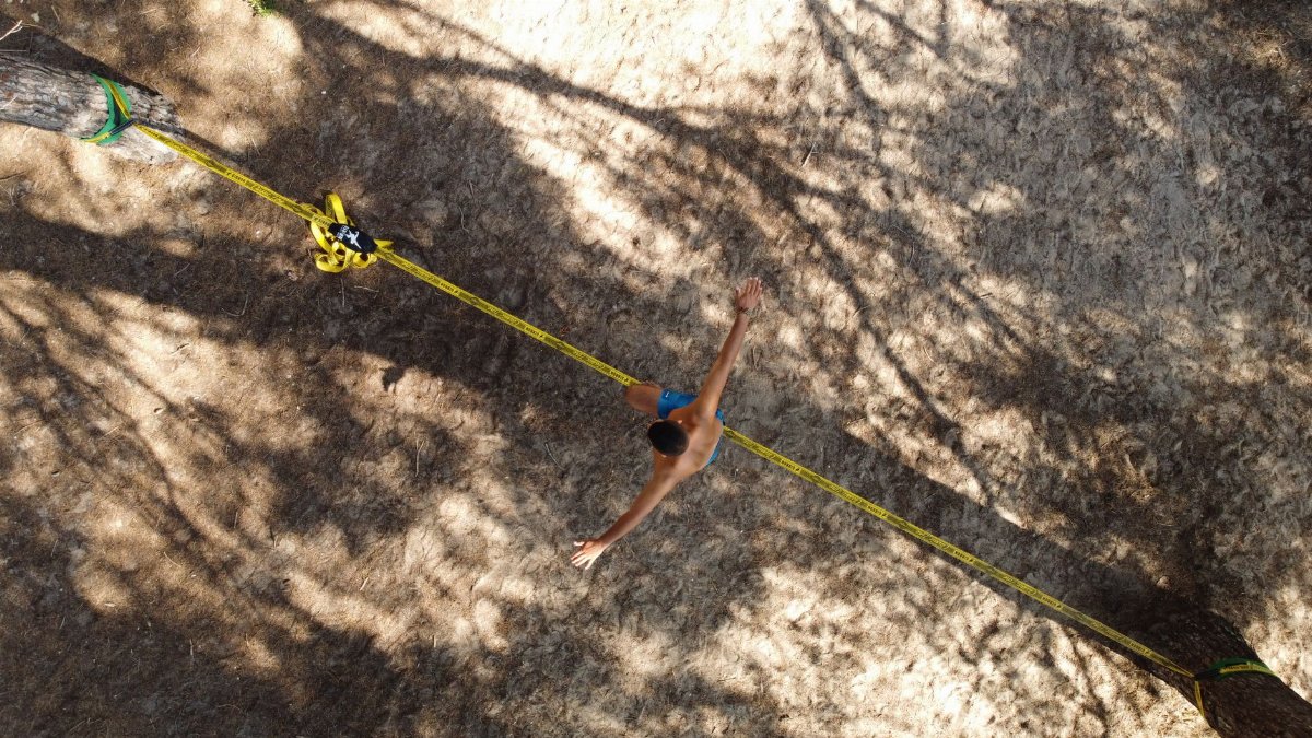 A drone captures a man skillfully balancing on a slackline outdoors in Tarragona, showcasing a thrilling beachside activity.