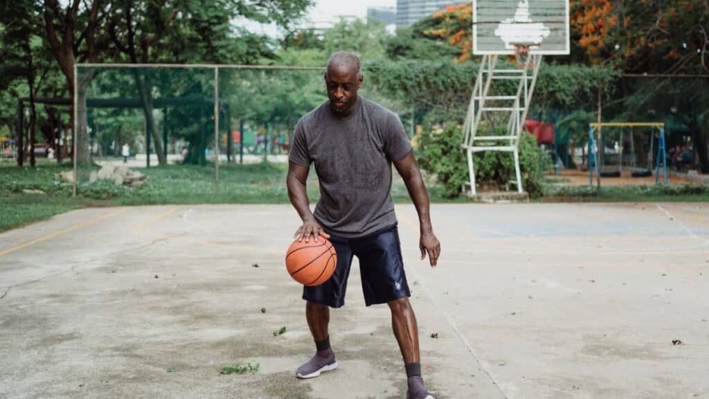 An adult man skillfully dribbles a basketball on an outdoor court in a park setting.