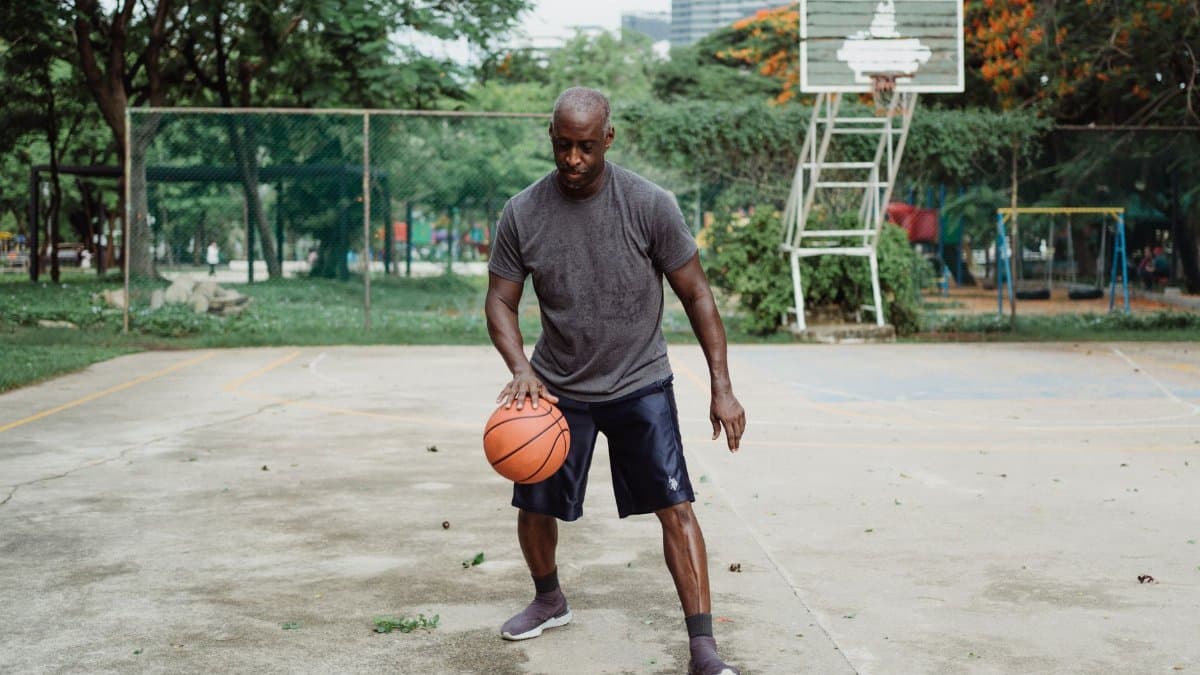 An adult man skillfully dribbles a basketball on an outdoor court in a park setting.