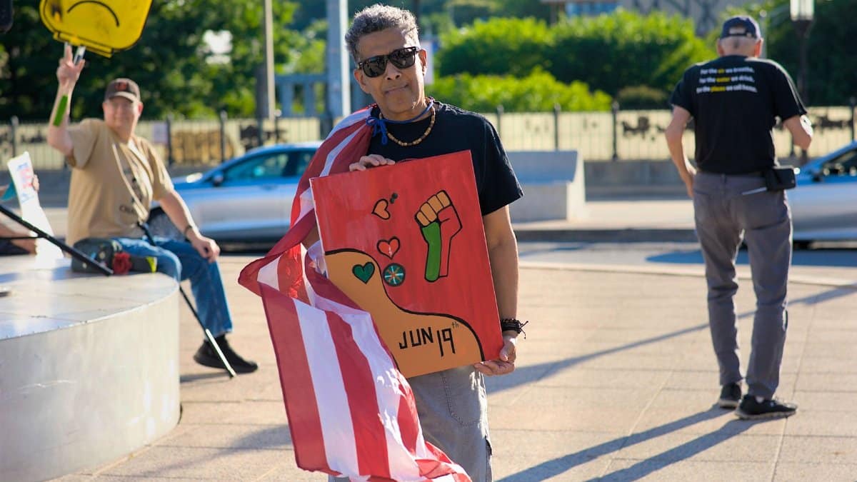 Protesters in Baltimore celebrate Juneteenth with signs and American flag, promoting democracy and freedom.