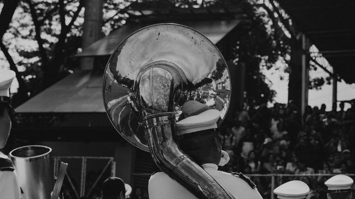 A monochrome view of a marching band playing at an outdoor event, showcasing shiny instruments and uniforms.