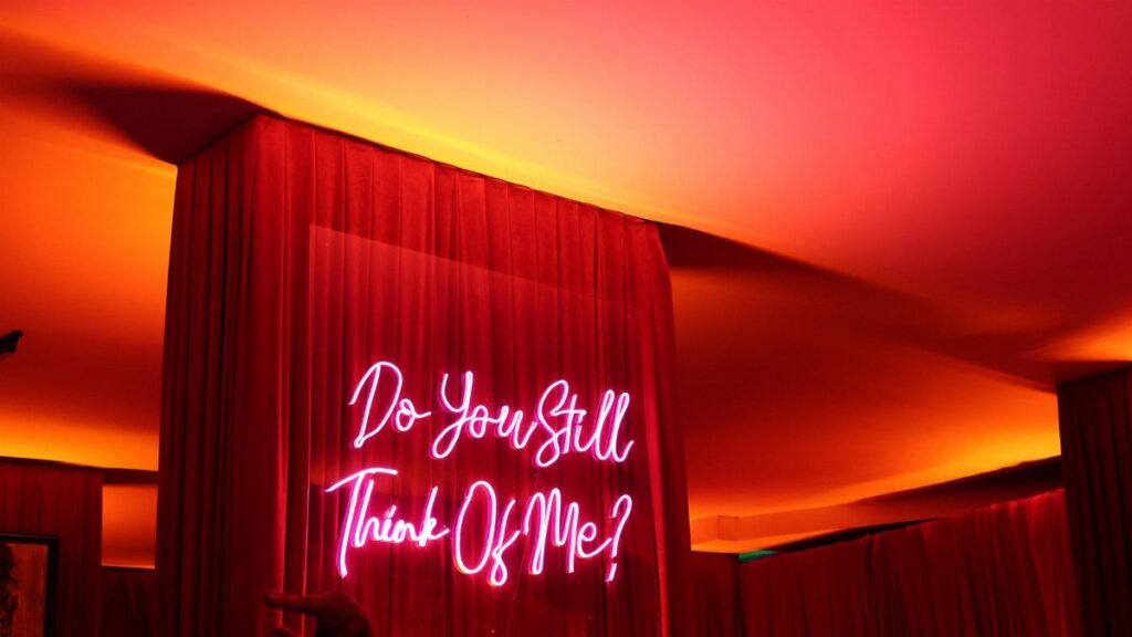 Vivid neon sign 'Do You Still Think Of Me?' with moody ambiance.
