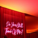 Vivid neon sign 'Do You Still Think Of Me?' with moody ambiance.
