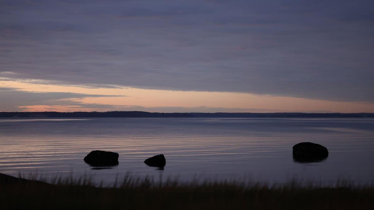 Peaceful evening lake view with silhouetted rocks and a colorful sunset sky.