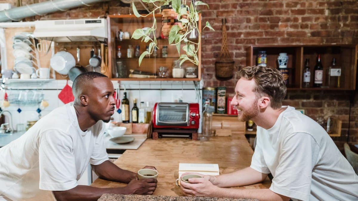 Two men enjoying a casual coffee conversation in a rustic kitchen setting.