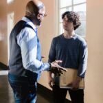 A high school teacher and student having a conversation in a brightly lit hallway.