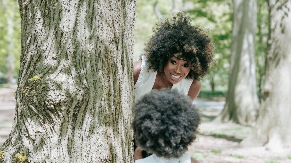 A joyful mother and child playing hide and seek behind a tree in a sunny park, showcasing happiness and connection.