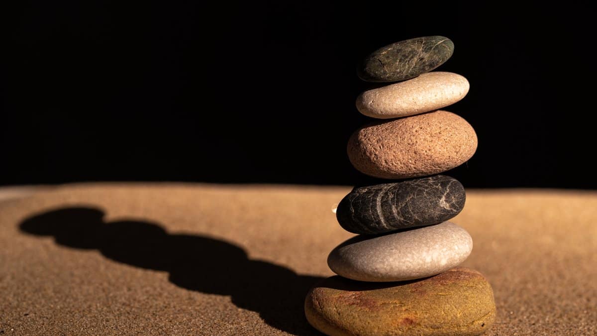 A stack of balanced pebbles on sand against a dark background symbolizing balance and harmony.