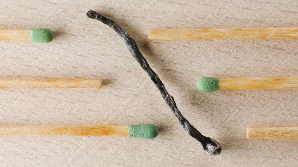 Charred match surrounded by green-tipped matches symbolizing burnout and contrast.