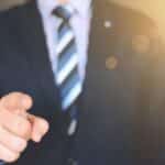 Confident businessman in a suit pointing forward, signifying leadership and focus.