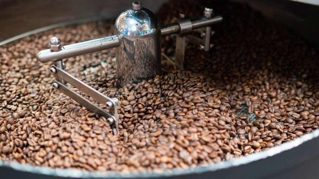 Close-up of coffee beans being roasted in a metal roaster, highlighting freshness.