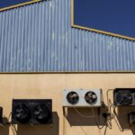 Exterior view of industrial air conditioning units mounted on a warehouse wall under clear blue sky.