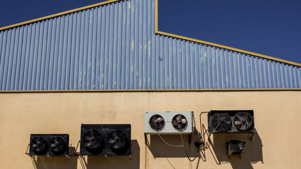 Exterior view of industrial air conditioning units mounted on a warehouse wall under clear blue sky.