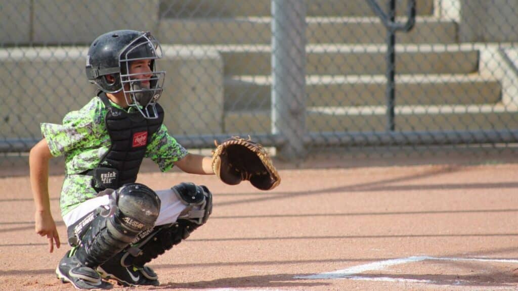 Young boy playing as a baseball catcher, crouched and ready during a daytime game.